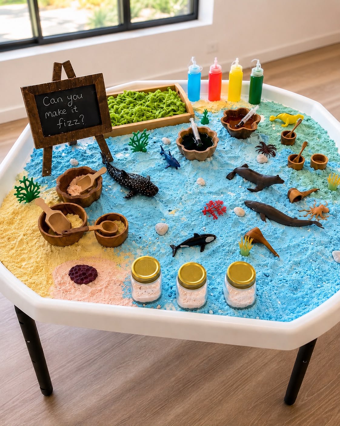 An ocean-themed Little Hands Sensory tray with a 'Can you make it fizz?' chalkboard, coloured foam, toy sea creatures, wooden bowls and colour bottles